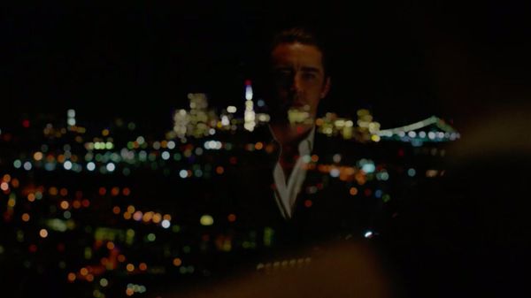 A man's reflection can be seen in a window. He is looking out over the city of San Francisco, which is blurry and lit up in the background.