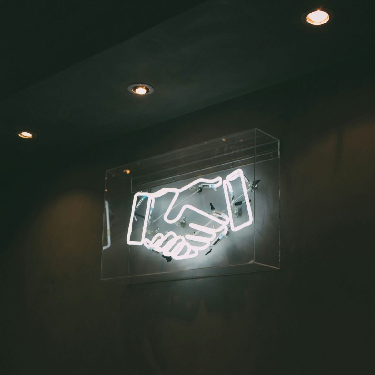 Neon handshake sign on dark wall, symbolising brand partnership and deal negotiation