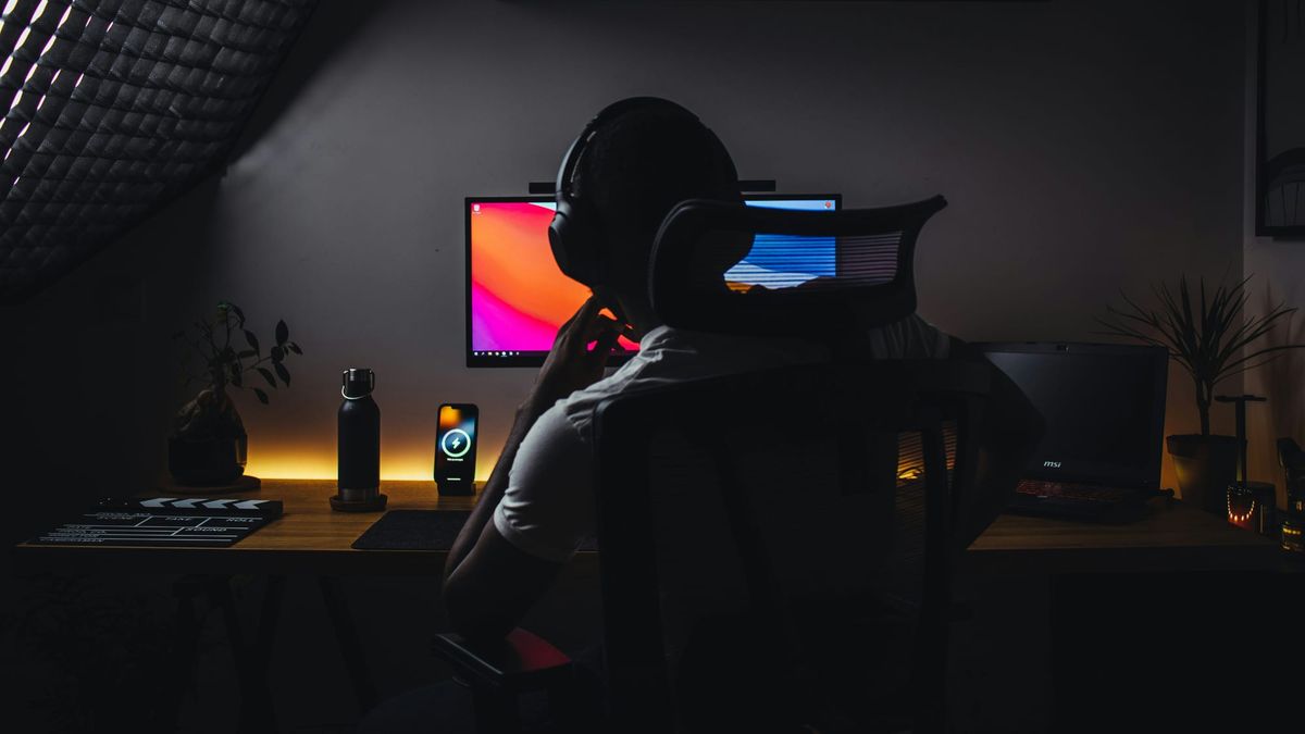 Creator at desk wearing headphones, focused on colorful monitor displaying analytics or content, surrounded by streaming setup and equipment