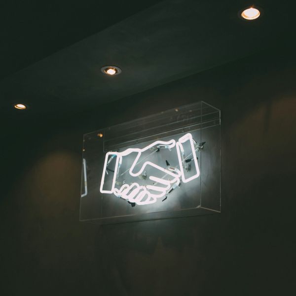 Neon handshake sign on dark wall, symbolising brand partnership and deal negotiation