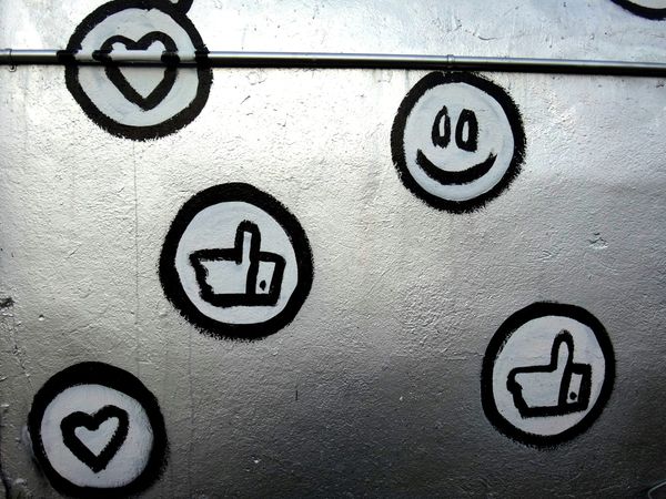 Street art showing hand-drawn emoticons including heart, smiley face, and thumbs up on white wal