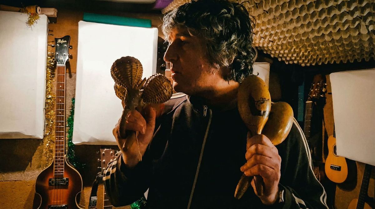 SUPER 8 musician Paul 'Trip' Ryan holding maracas in his home recording studio surrounded by guitars and acoustic panels during the Retro Metro sessions