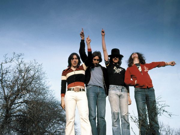 Four members of Unicorn pose outdoors beneath a blue sky in a colour photograph by Hipgnosis.