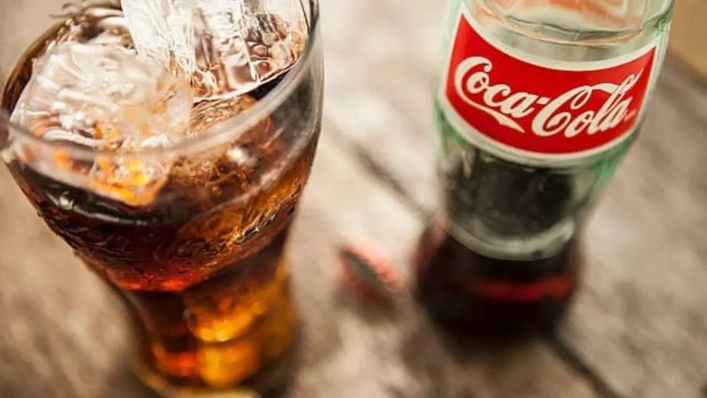 Un verre de Coca-Cola avec des glaçons et une bouteille de Coca-Cola sur une table en bois.