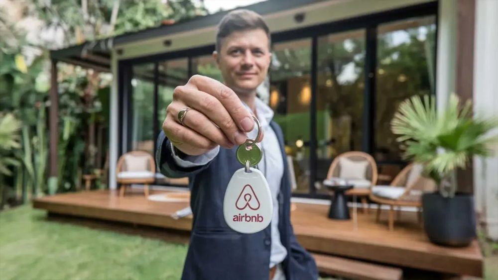 Un homme souriant tenant une clé Airbnb devant une maison moderne, symbolisant l'impact des nouvelles lois sur les locations de courte durée.