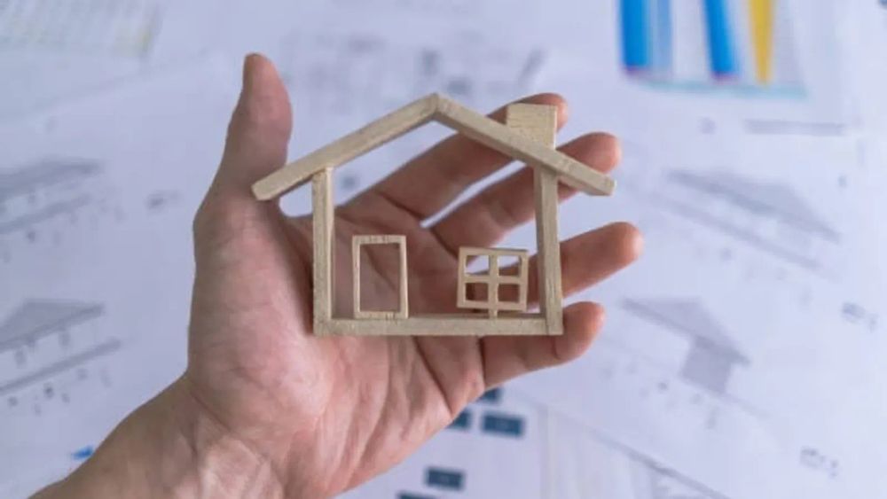 Une main tenant une maquette de maison en bois, symbolisant l'investissement immobilier neuf.