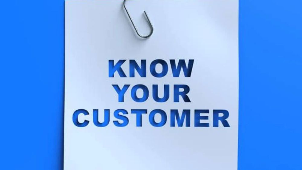 Un papier blanc avec un trombone et le texte "Know Your Customer" découpé en bleu.