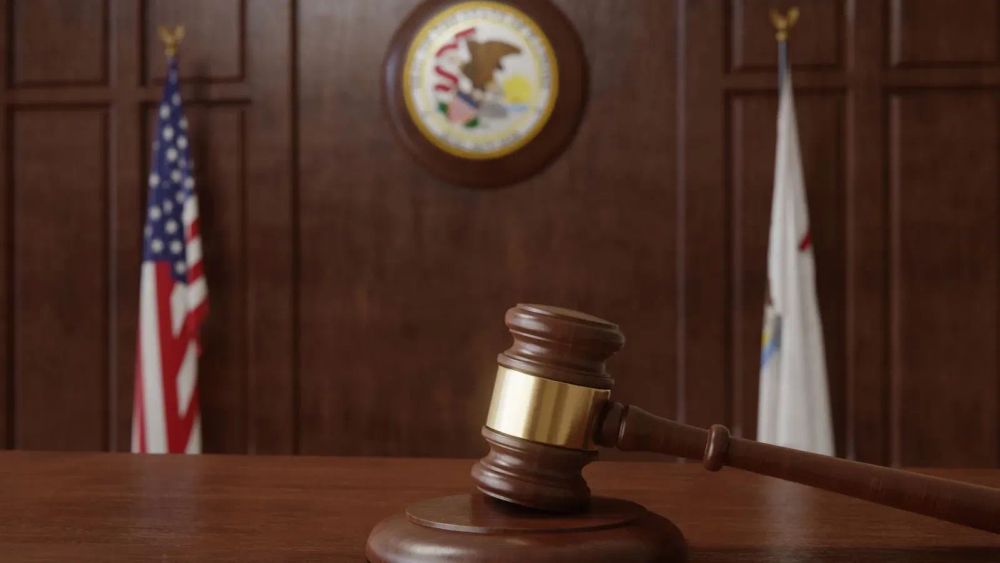 Un marteau de justice sur un bureau en bois, avec des drapeaux américain et d'état en arrière-plan.