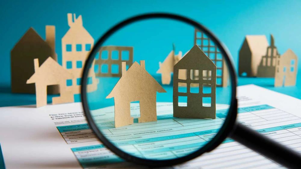 Loupe grossissant des maquettes de maisons en carton sur un document, symbolisant l'analyse et la recherche d'opportunités dans le secteur de l'immobilier.