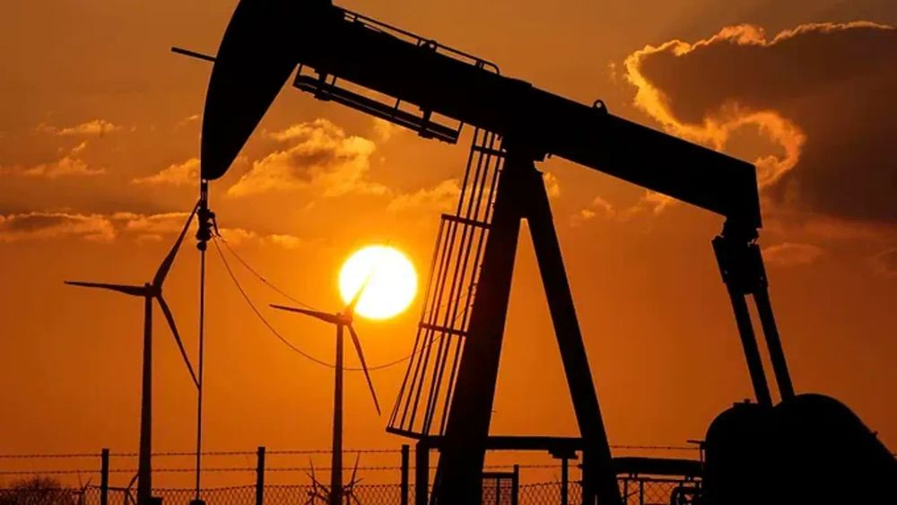 Silhouette d'un puits de pétrole et d'éoliennes au coucher du soleil, symbolisant le contraste entre les énergies fossiles et renouvelables.