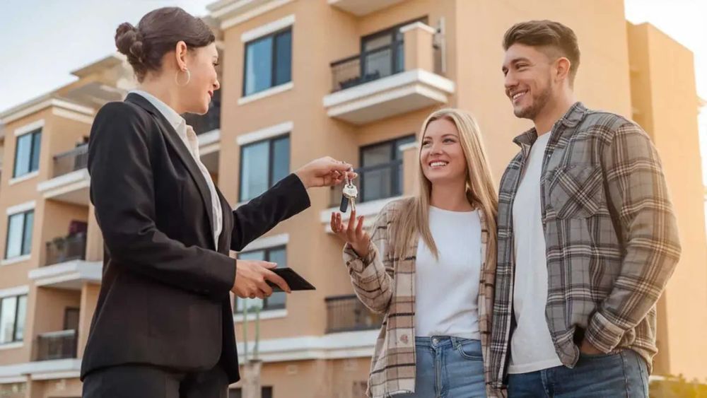 Un couple reçoit les clés de son nouveau logement des mains d'une agente immobilière.