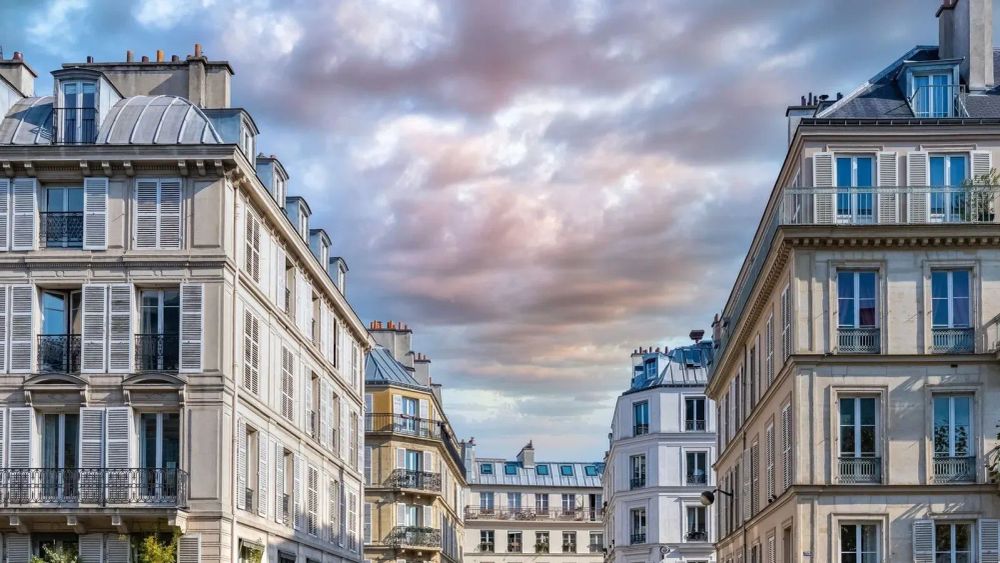 Immeubles parisiens typiques avec des fenêtres à volets et des toits en zinc sous un ciel nuageux.