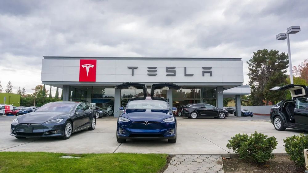 Un concessionnaire Tesla avec plusieurs voitures exposées devant, dont une avec les portes papillon ouvertes.