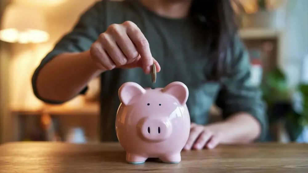 Une personne insère une pièce dans une tirelire rose en forme de cochon.