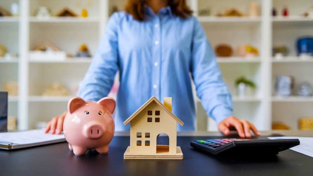 Épargne pour l'immobilier : tirelire, maison miniature et calculatrice sur un bureau, symbolisant l'investissement et la planification financière.