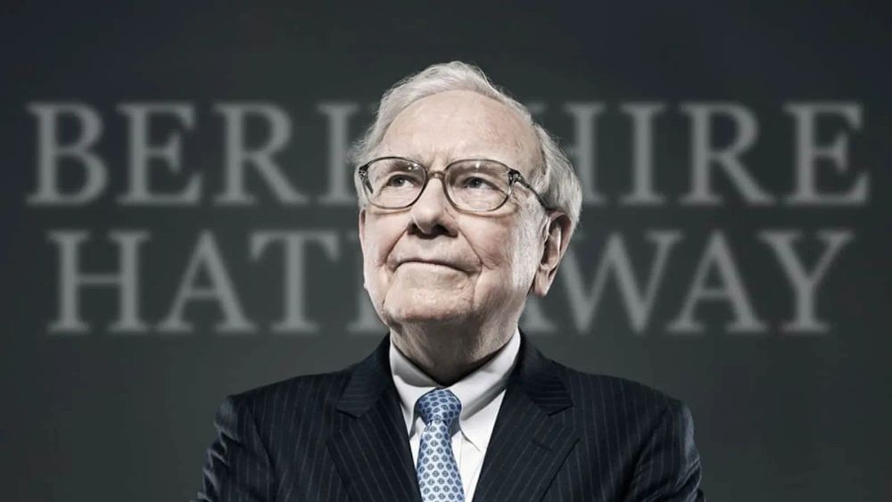 Warren Buffett, PDG de Berkshire Hathaway, portant des lunettes et un costume rayé, avec le nom de sa société en arrière-plan.