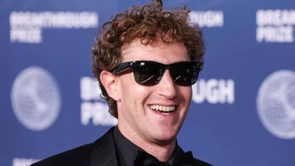 Mark Zuckerberg souriant, portant des lunettes de soleil et un costume noir, devant un fond bleu avec le texte 'Breakthrough Prize'.