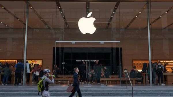 Magasin Apple avec le logo lumineux de la marque au-dessus de l'entrée, des clients à l'intérieur et des passants à l'extérieur.