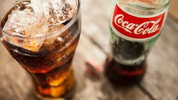 Un verre de Coca-Cola avec des glaçons et une bouteille de Coca-Cola sur une table en bois.