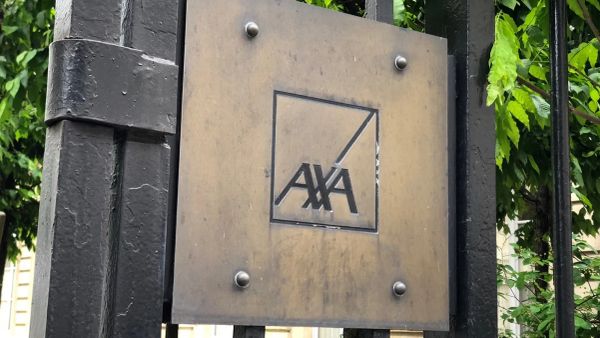 Logo AXA sur une plaque en métal fixée à une grille noire, entourée de verdure.