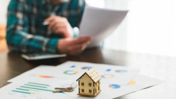 Un homme examine des documents financiers avec une maquette de maison et des clés, symbolisant l'investissement immobilier locatif.