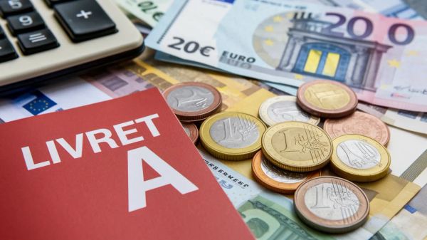 Un Livret A rouge est posé sur des billets et des pièces en euros, avec une calculatrice en arrière-plan.