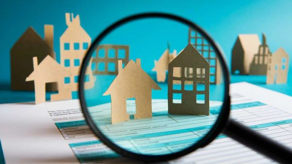 Loupe grossissant des maquettes de maisons en carton sur un document, symbolisant l'analyse et la recherche d'opportunités dans le secteur de l'immobilier.
