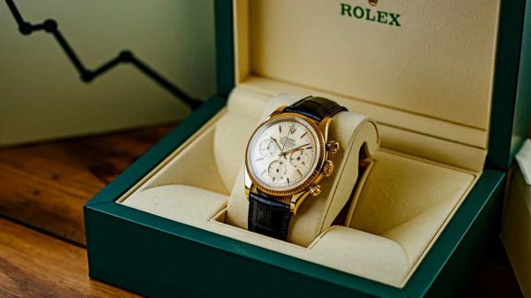 Une montre Rolex en or avec un bracelet en cuir noir est présentée dans un écrin vert.