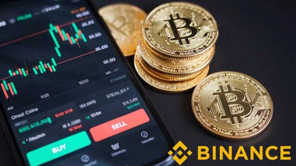 Image d'un téléphone affichant un graphique boursier, avec des pièces de Bitcoin et le logo Binance, illustrant le trading de cryptomonnaies.