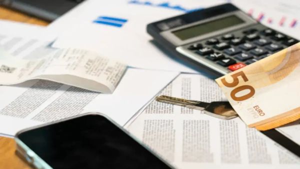 Une calculatrice, un billet de 50 euros, une clé et un téléphone portable sont posés sur des documents financiers.