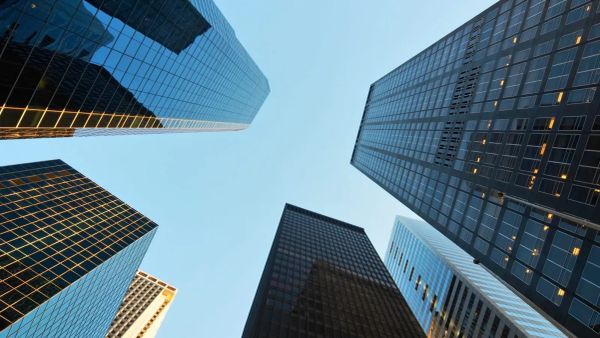 Vue plongeante sur des gratte-ciel reflétant le ciel bleu, symbolisant l'innovation et la modernité dans l'immobilier.
