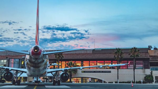Avion à l'aéroport de Toulon Hyères, ciel nuageux au coucher du soleil, bâtiment de l'aéroport en arrière-plan.
