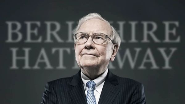 Warren Buffett, PDG de Berkshire Hathaway, portant des lunettes et un costume rayé, avec le nom de sa société en arrière-plan.