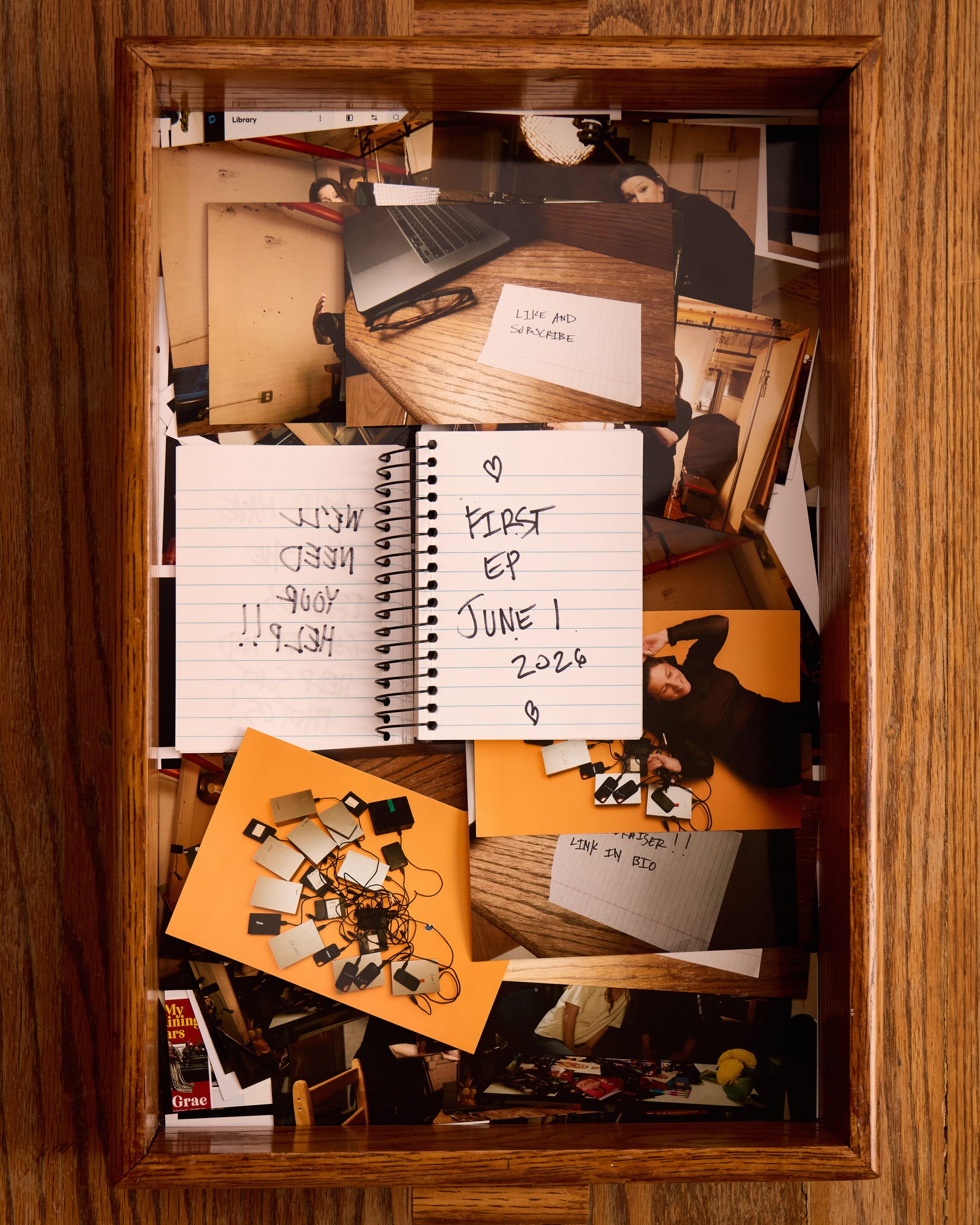The notebook now says “First episode June 1, 2026” In the tray of 4x6 photos, promo photos of Mindy Tucker surrounded by hard drives. 