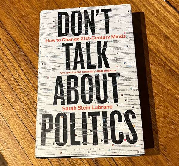 Photo of book on wooden benchtop. Book title in bold capital letters, with background lots of screenshots of tweets and suchlike