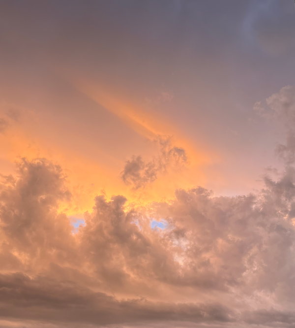 An ominous, post-storm sunset sky over Canberra. Light grey clouds swirling, tiny eyes of blue peeking through beneath pinky-yellow whisps