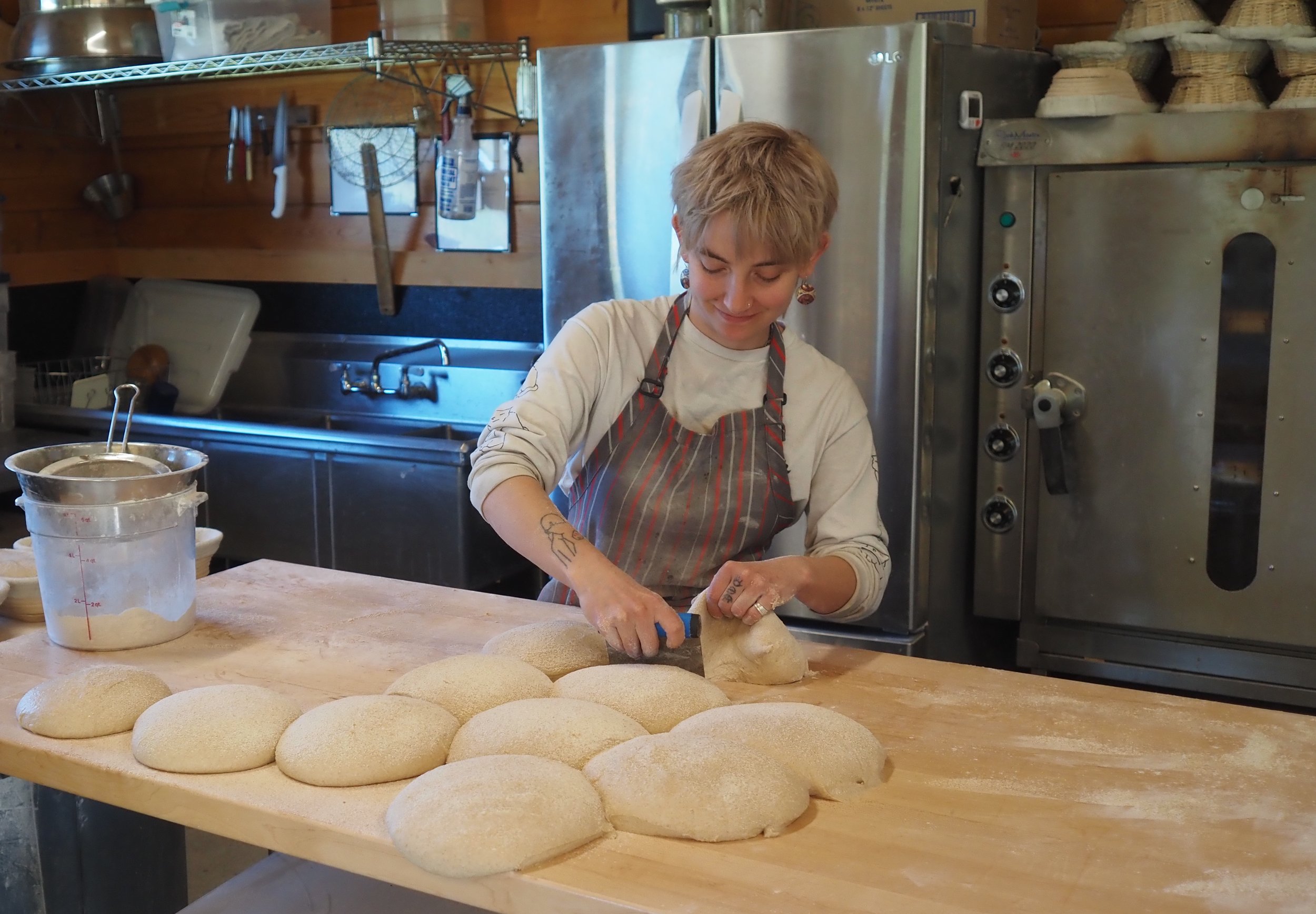   Caitlyn Faircloth readies loaves of Chimacum Valley Grainery’s Farmstead Sourdough made from grain grown within sight of where she stands. Beacon photo by Derek Firenze  