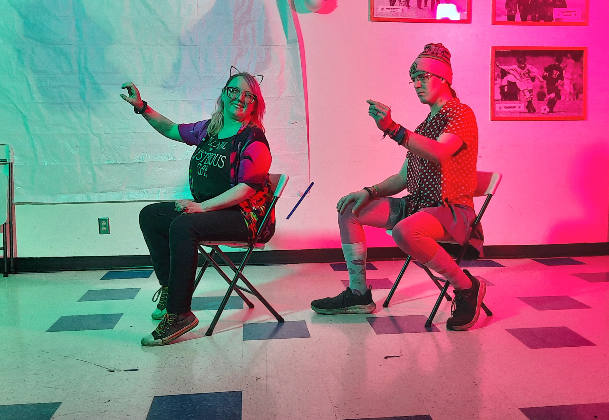 Andrea Dennison and Aiden Kinsella, Olympic Improv founders, play off of each other at improv practice. One person is sitting in a chair in front of the other and both people have their arms extended