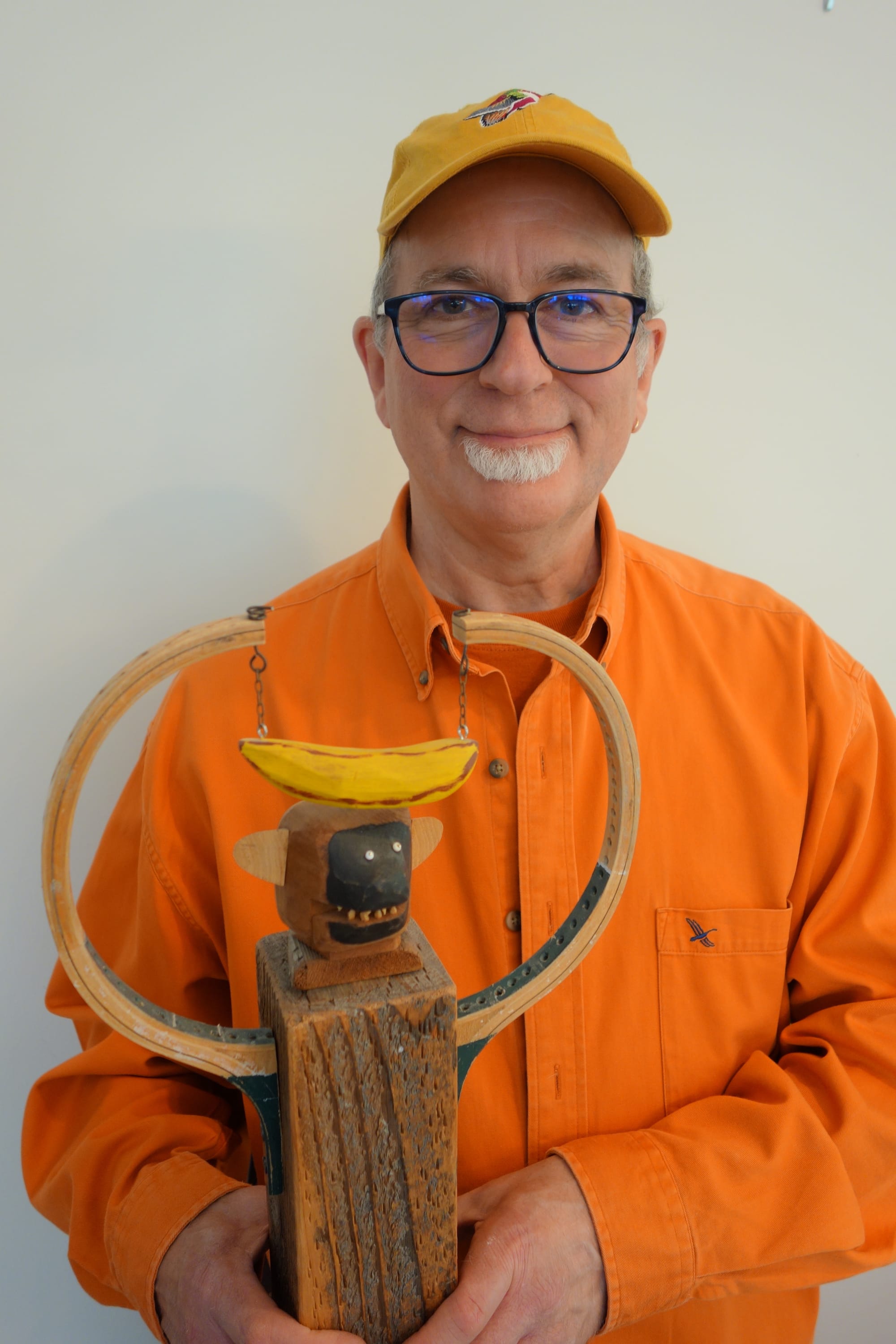 Sculptor Peter Koronakos with a monkey sculpture in a bright orange shirt 