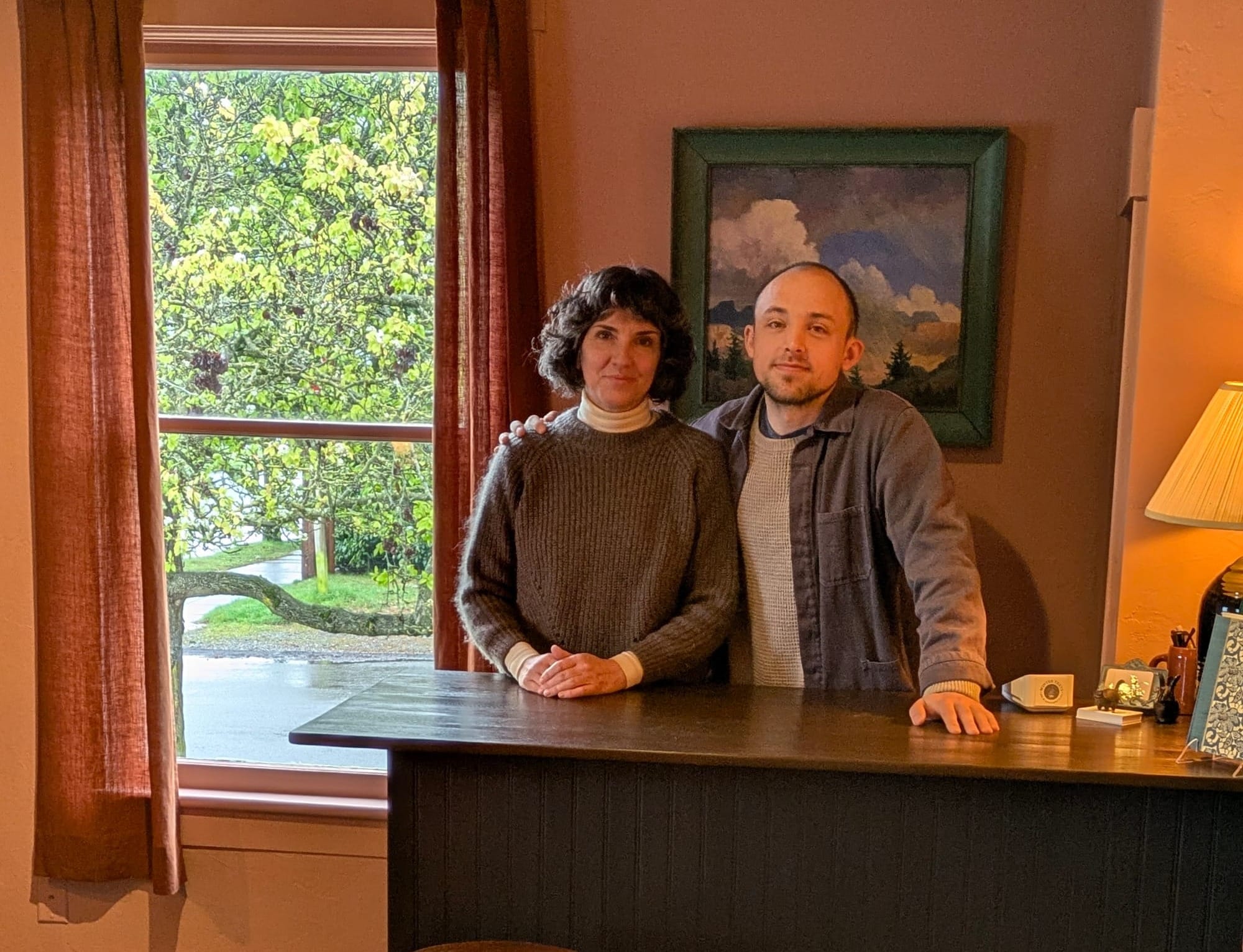 Connor Bouchard-Roberts and Camille Finefrock standing behind a brown counter with a window behind, left