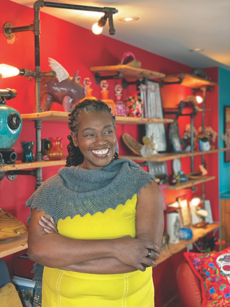 Photo of Stephanie Delaney in front of shelves of objects in a blue shawl and yellow dress.