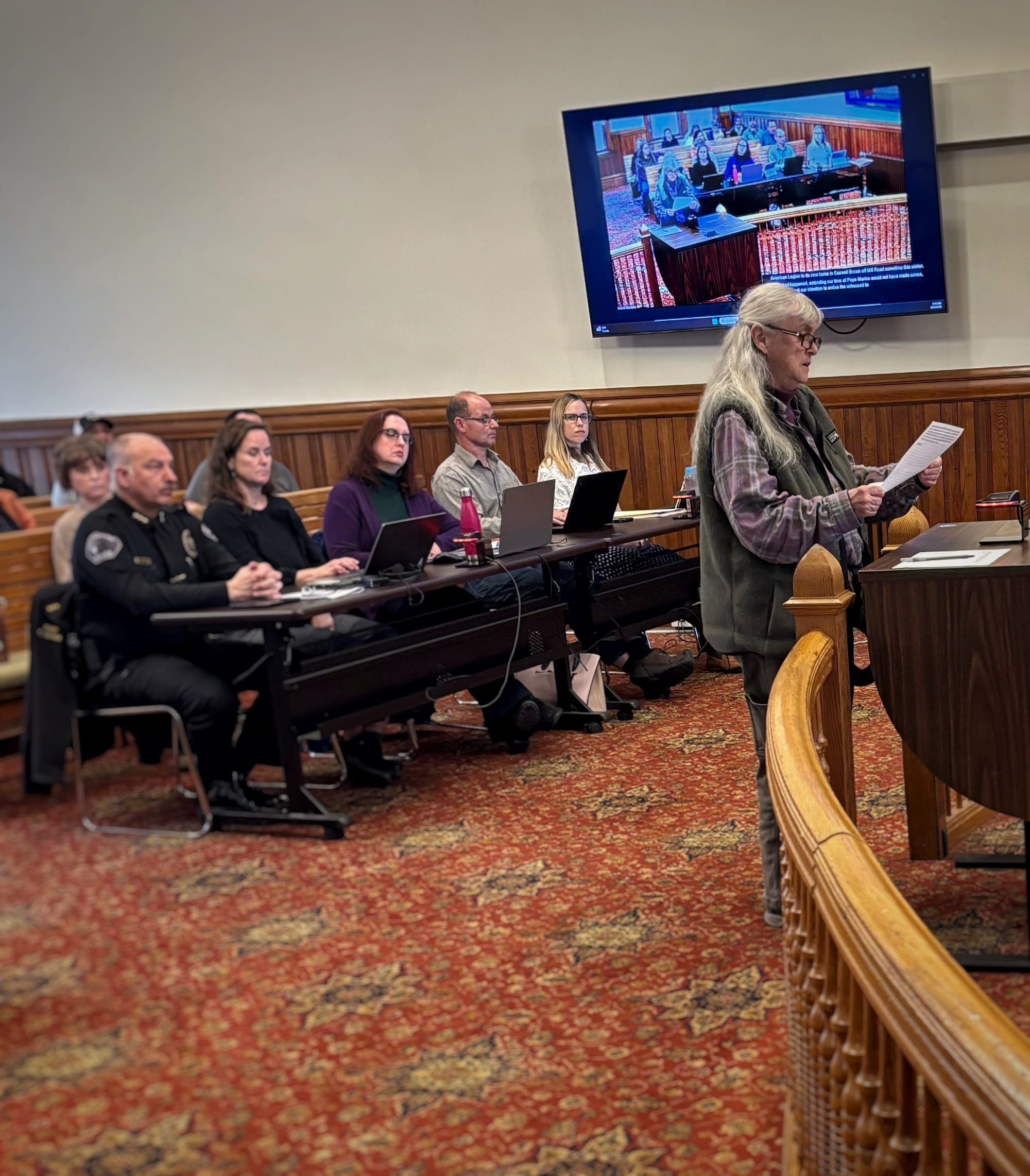 Julia Cochrane, right, at a lectern with her back to the city council audience.