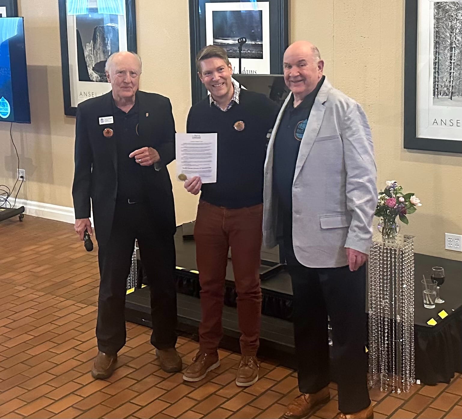 Terry Umbreit, David Faber, and Gary Keister in front of a small stage with a proclamation.