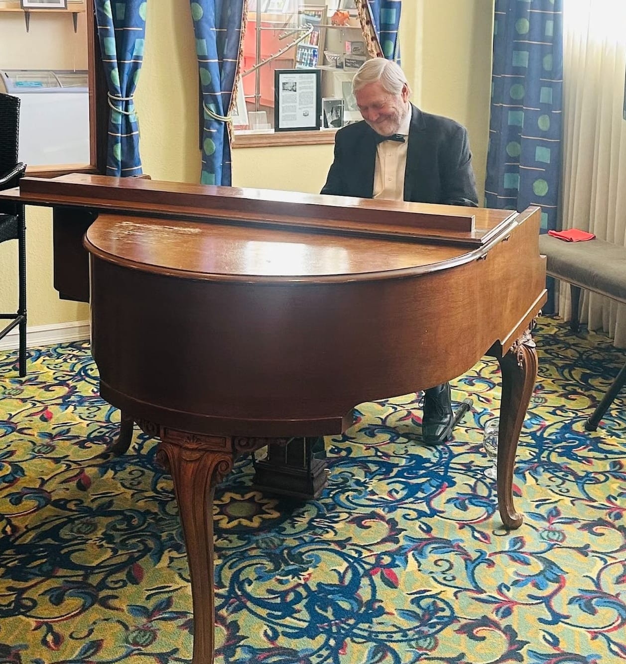 A piano player in a tuxedo playing a brown baby grand piano.
