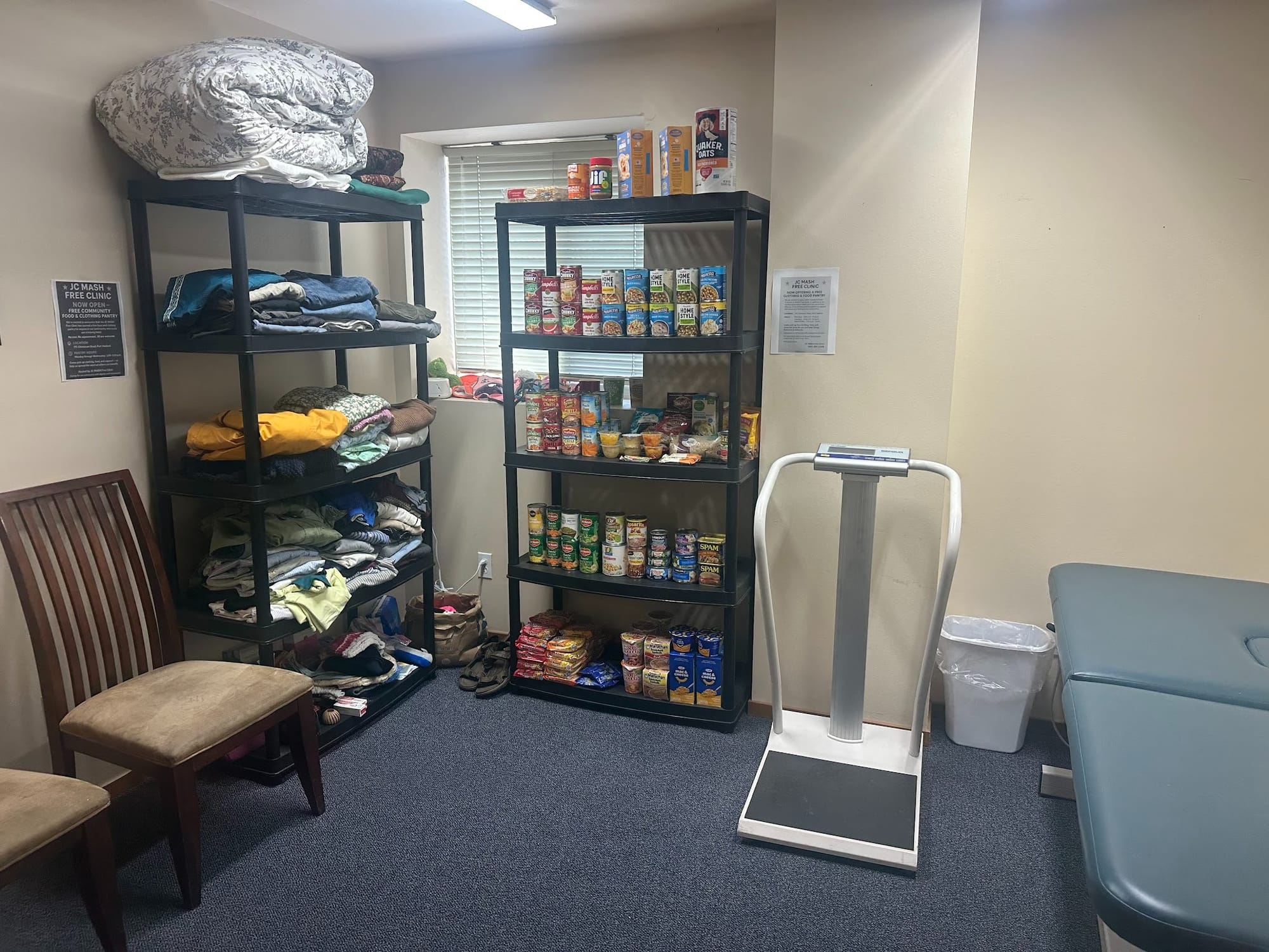 Two shelves one with blankets on the left, one with food at center, a scale and exam table sit at right. 