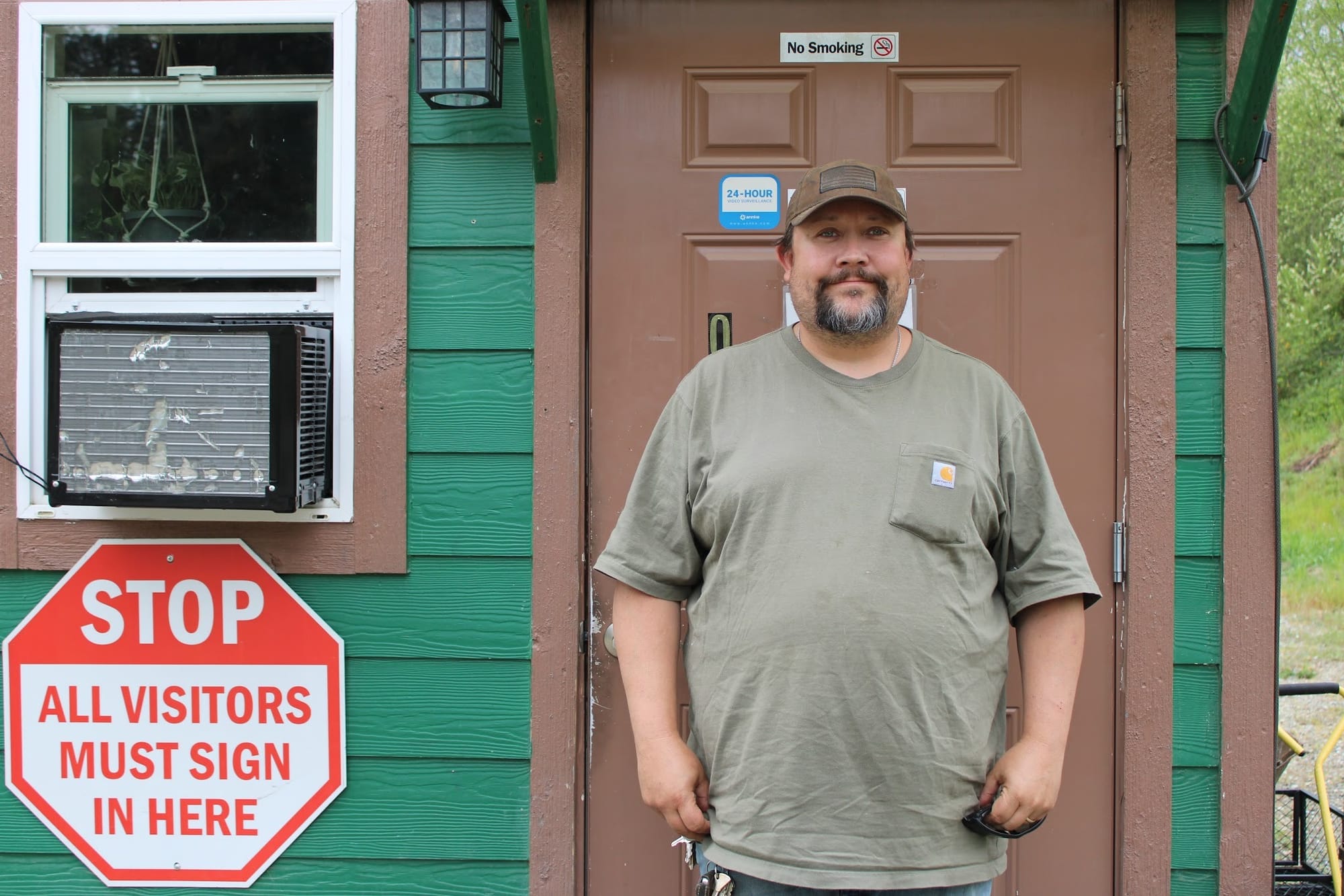 Jacob Powell, standing in front of the site's office with green siding and a brown door. 