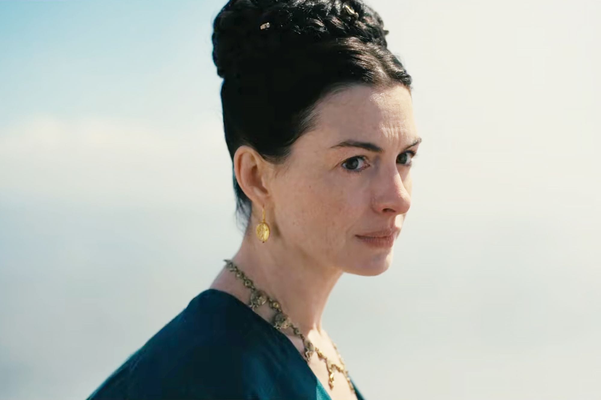 Anne Hathaway is Penelope with a gold necklace and earrings and her hair braided up.
