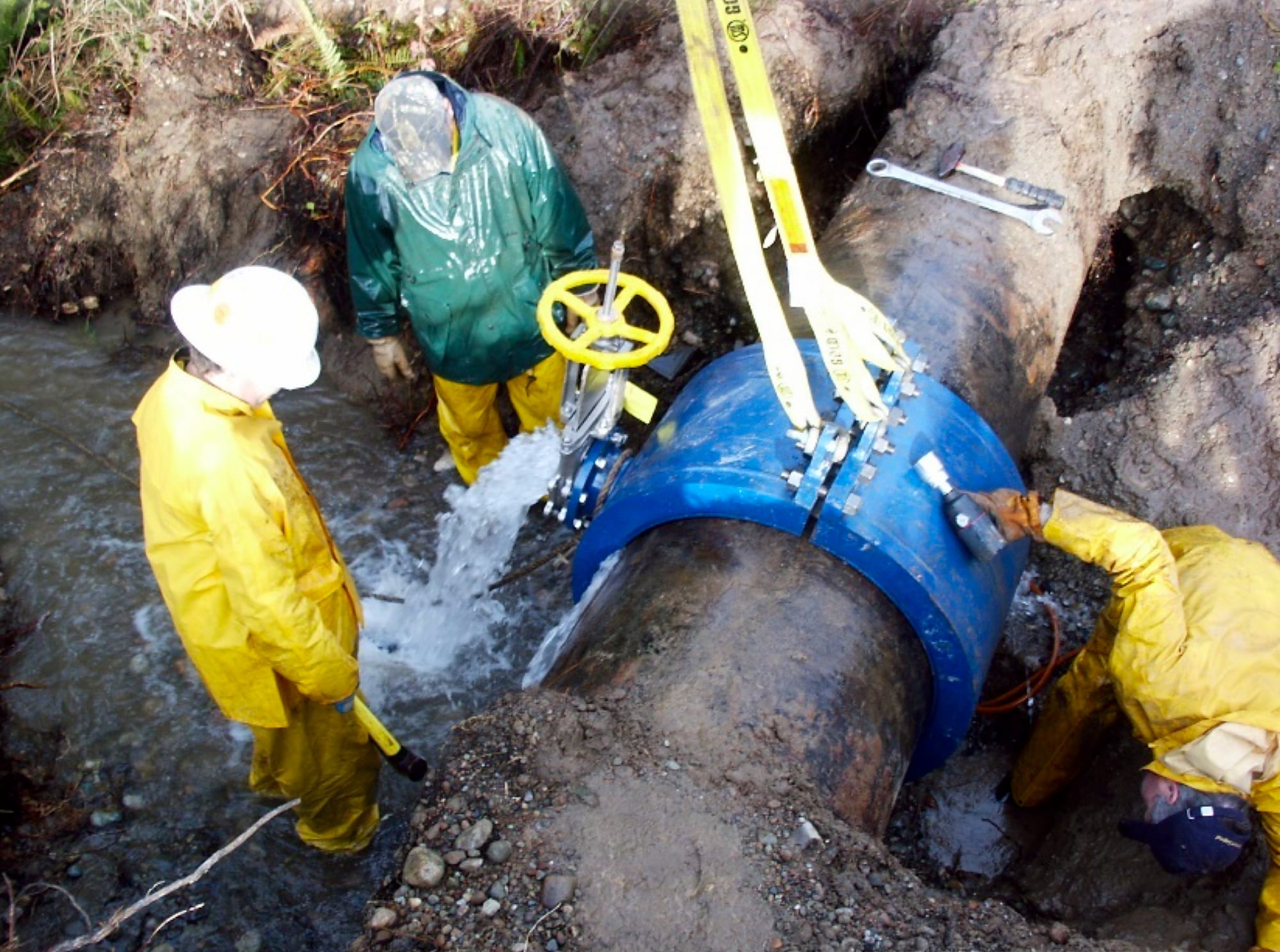 Workers in rain gear standing in water making an emergency repair on a pipeline break. 