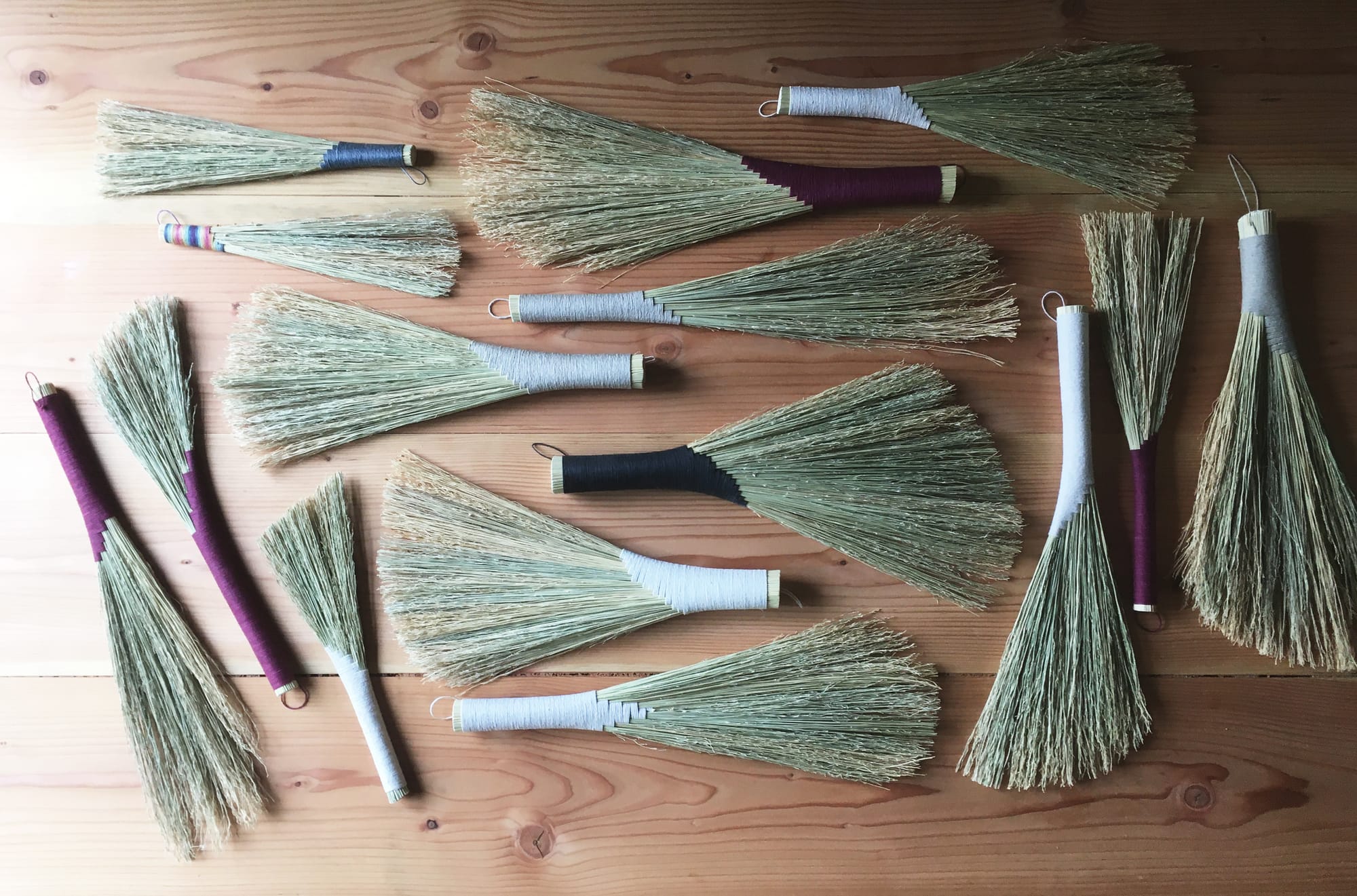  15 “Turkey wing” hand brooms on a wood table top.