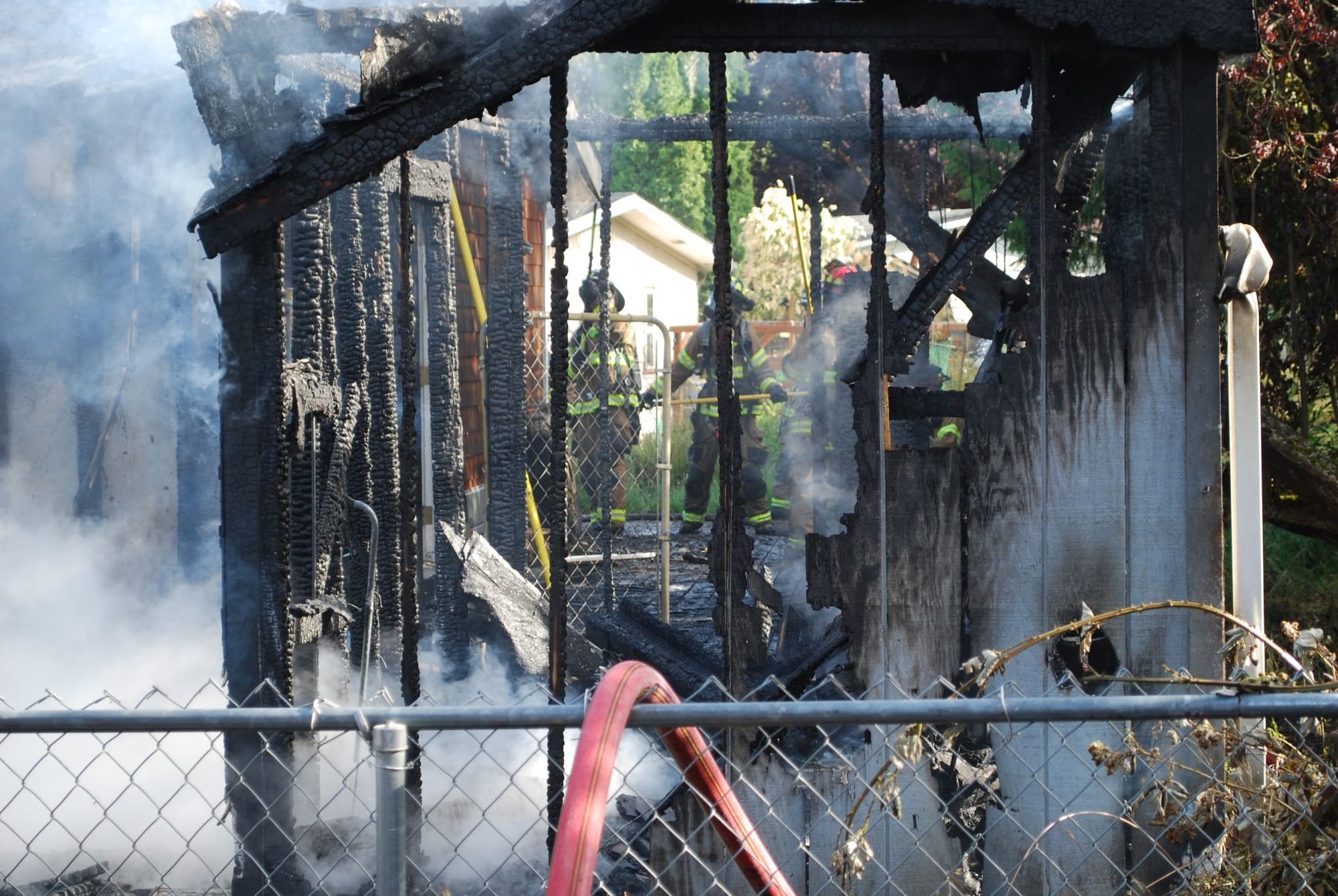 The smoldering remains of a burnt residence with firefighters in the background.